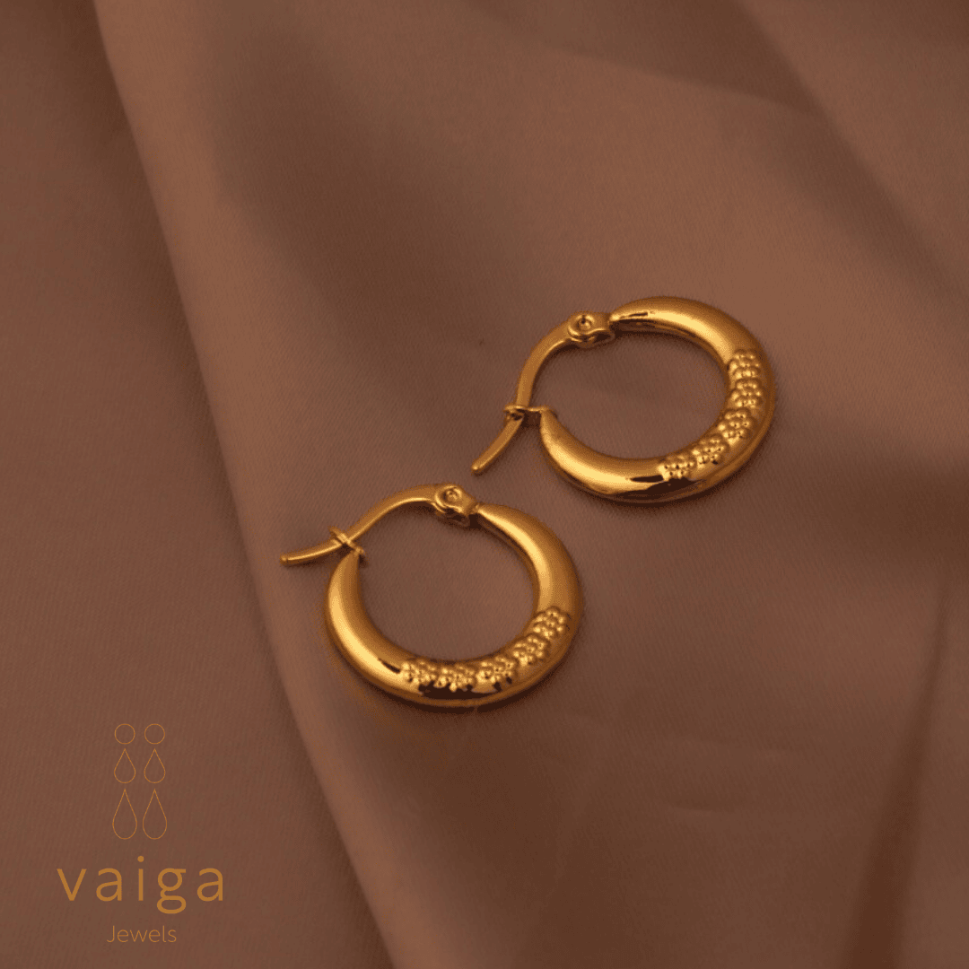 Gold-toned stainless steel textured hoop earrings design by Vaiga Jewels, modern luxury women's accessory on blush pink background.