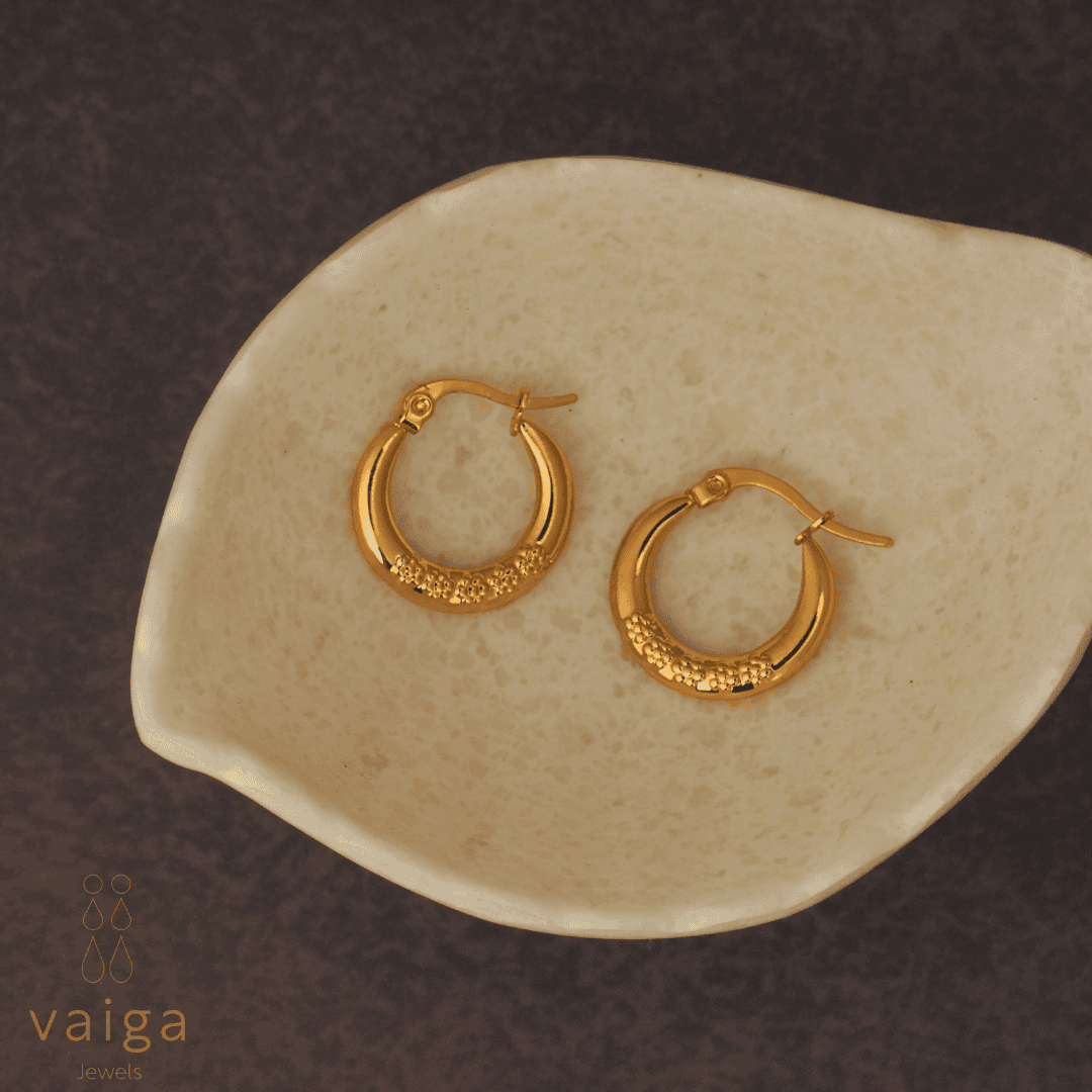 Gold-toned stainless steel textured hoop earrings design by Vaiga Jewels, modern luxury women's accessory placed in a white shell shaped dish .