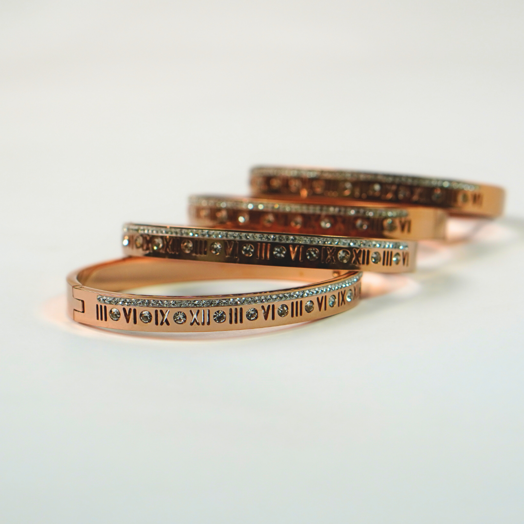 Stainless steel bracelets with roman numeral design stacked on a white surface