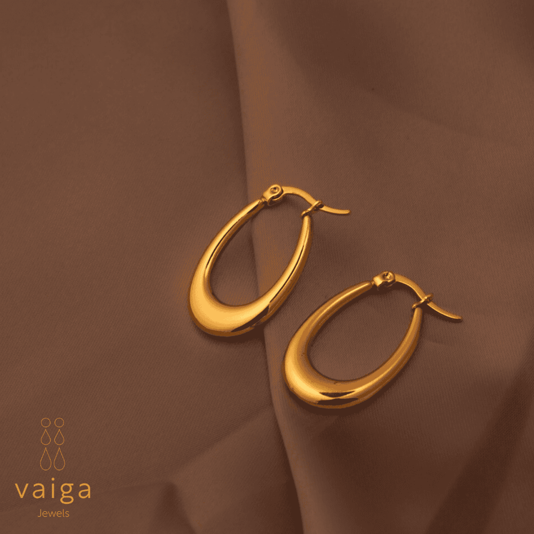 Gold-toned stainless steel tear drop - shaped earrings by Vaiga Jewels, modern luxury women's accessory on blush pink background.