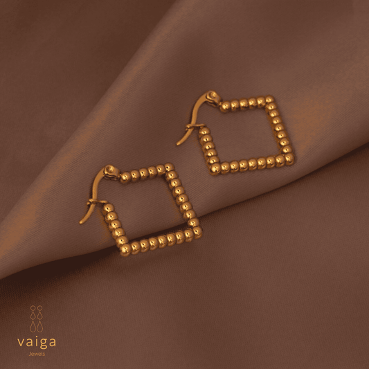 Gold-toned stainless steel textured square - shaped earrings by Vaiga Jewels, modern luxury women's accessory on blush pink background.