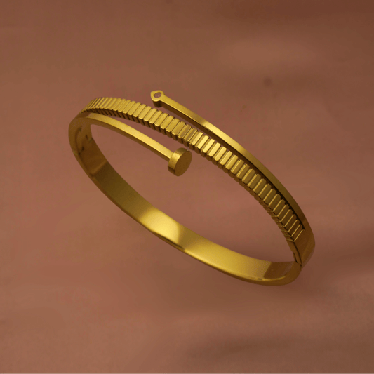 Gold-toned stainless steel bracelet with screw-nail inspired design by Vaiga Jewels, modern luxury women's accessory on blush pink background.
